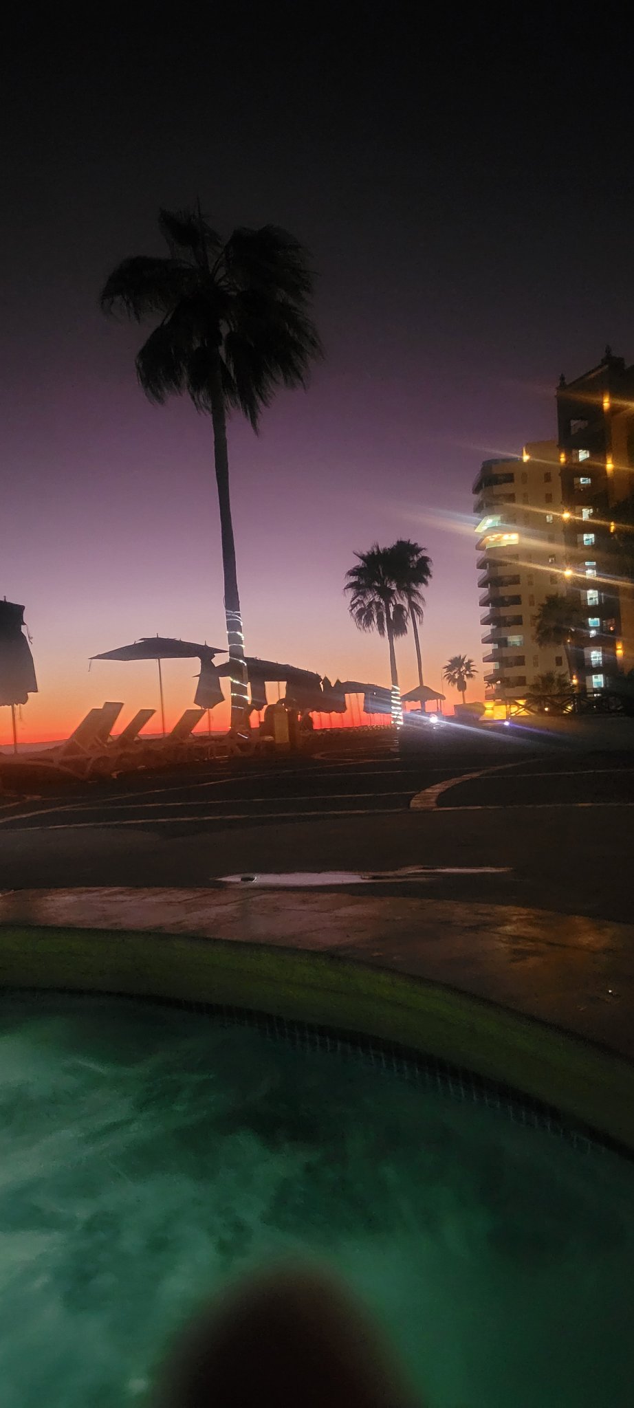 Resort pool glowing beneath a purple and orange evening sky