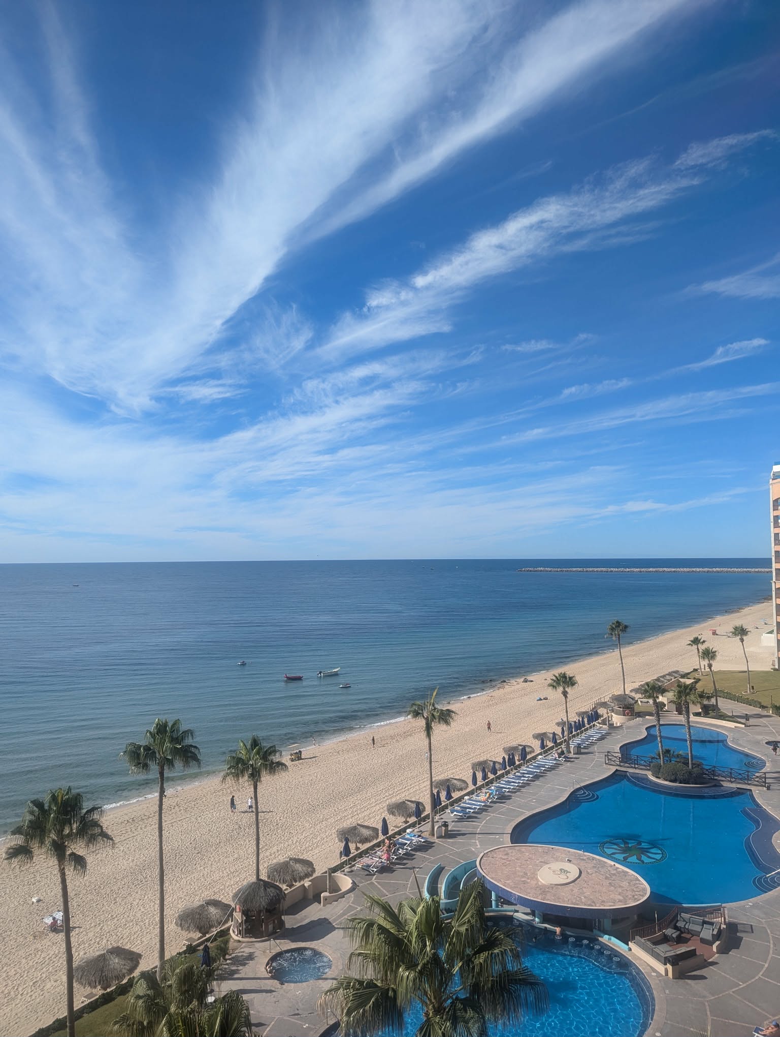 Elevated view of resort pools, sandy beach and the Sea of Cortez beneath streaked clouds